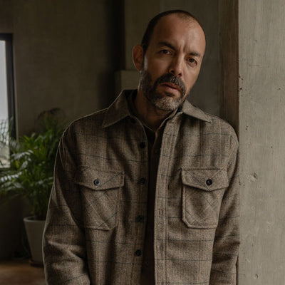 Man in the Aberdeen Wool Twill Shirt Jac in Thistle Grove standing by a concrete wall