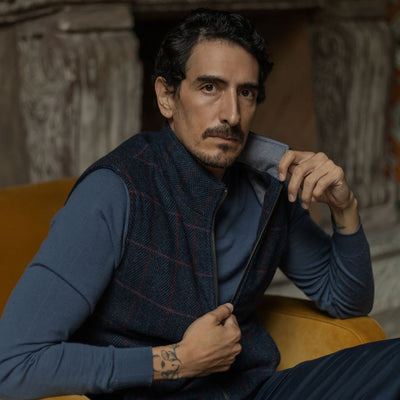 Man in the Ashton Wool Herringbone Vest in Clan Blue in an armchair, adjusting the collar