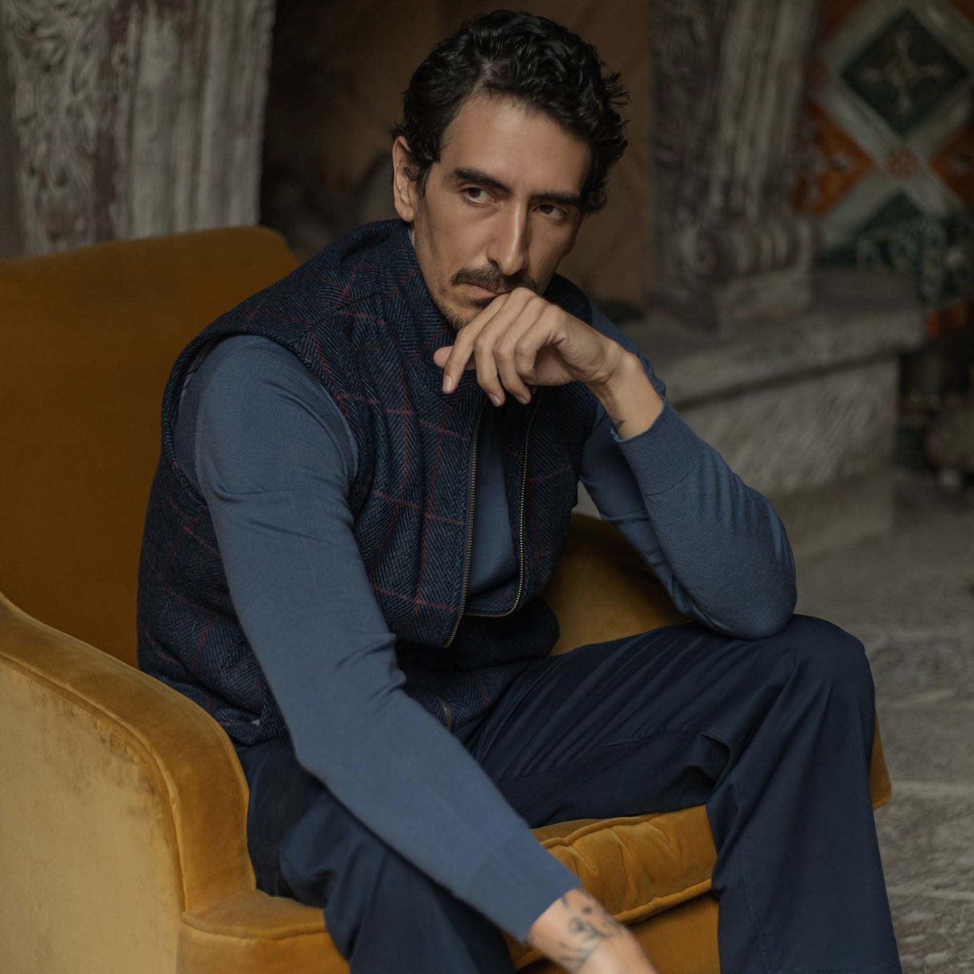 Man in the Ashton Wool Herringbone Vest in Clan Blue seated in an armchair, hand at his chin