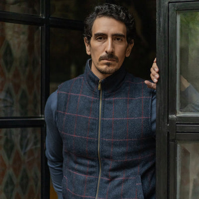 Man in the Ashton Wool Herringbone Vest in Clan Blue standing at a dark steel window