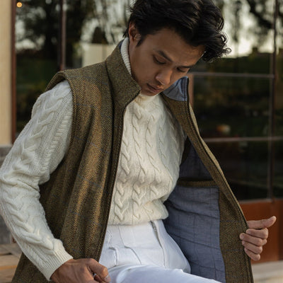 Man in the Ashton Wool Herringbone Vest in Mosswood and white trousers seated on a bench