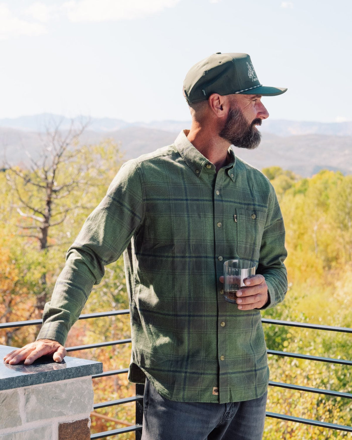 Man in a green plaid flannel shirt on a deck overlooking autumn hills
