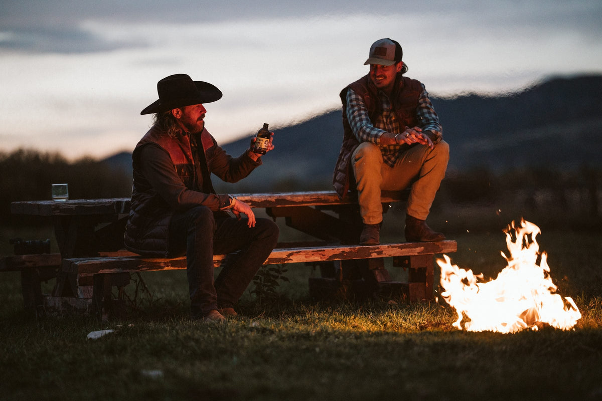 Two men talking by a campfire at dusk in the mountains