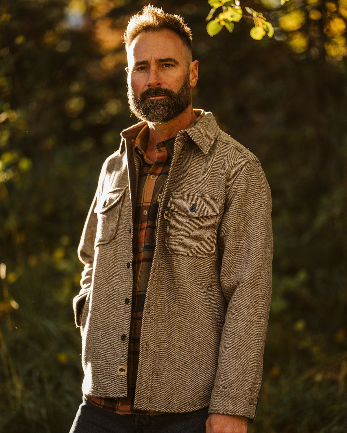 Man in a herringbone wool jacket over a plaid flannel in autumn light