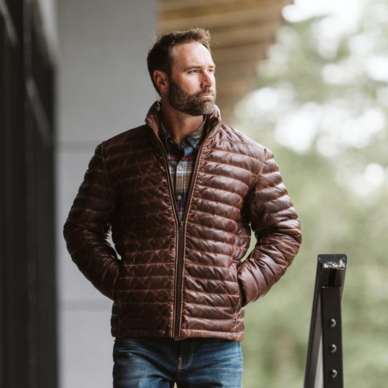 Man wearing a brown quilted jacket, standing outdoors with a thoughtful expression.