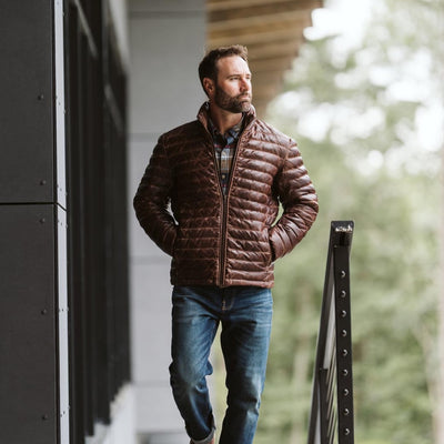 Outdoorsman dressed in a brown puffer jacket and plaid shirt, walking and looking pensive.