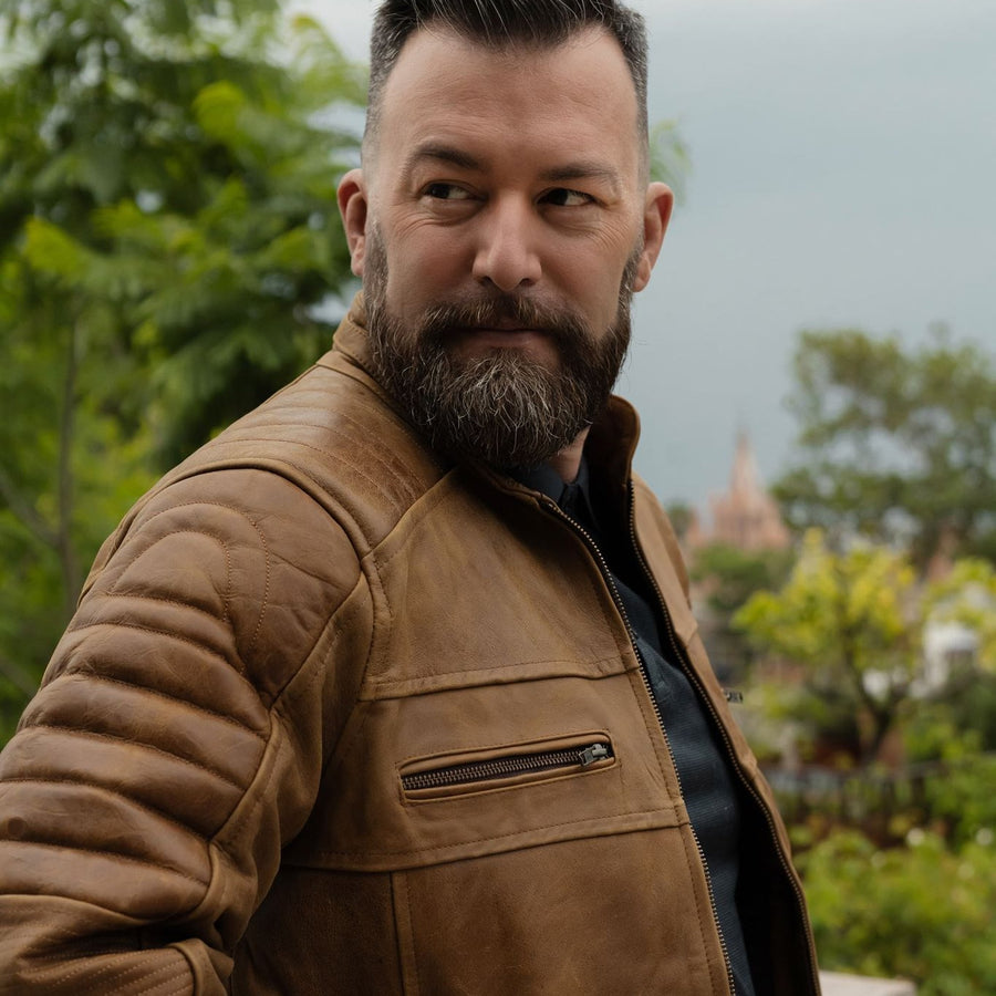 Bearded man in the Cafe Racer Leather Jacket in Distressed Tan on a garden balcony.