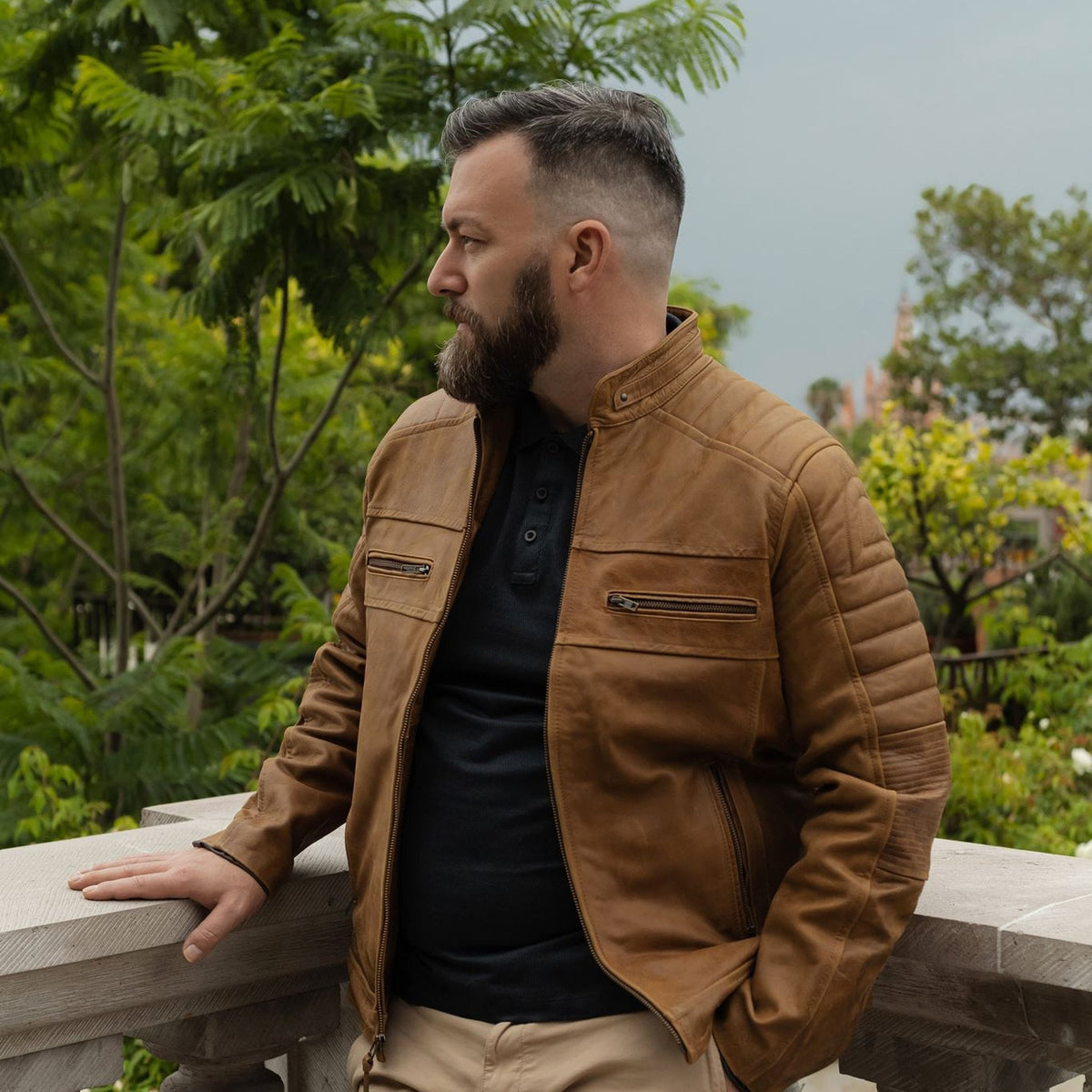 Man leaning on a stone balustrade in the Cafe Racer Leather Jacket in Distressed Tan.