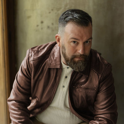 Man seated in the Glenwood Leather Driving Jacket in Mahogany Brown, worn open over a cream henley.