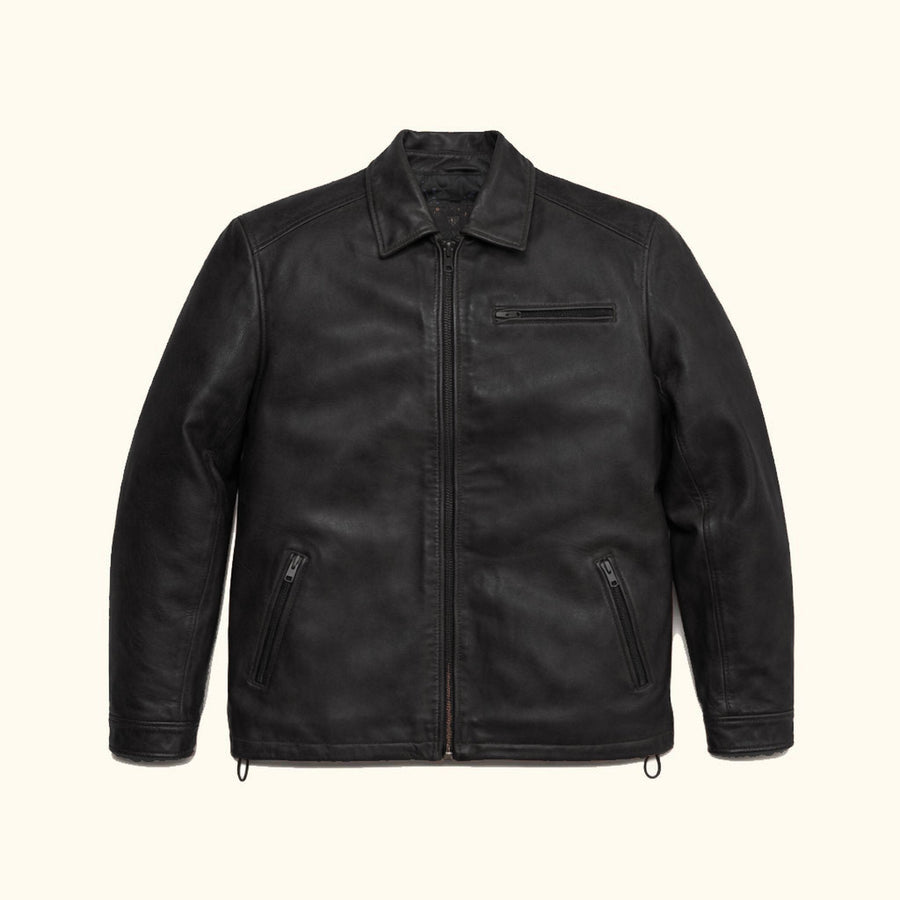 Man seated in the Glenwood Leather Driving Jacket in Vintage Black in a green-walled sitting room.