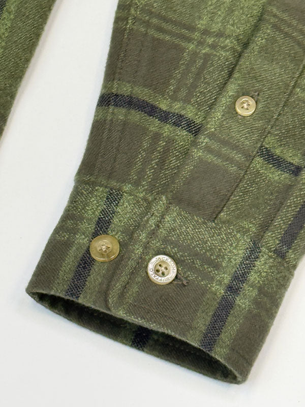 Close-up of a green plaid flannel shirt sleeve with dark stripes and brown buttons on a white background.