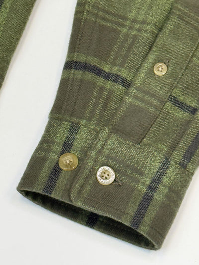 Close-up of a green plaid flannel shirt sleeve with dark stripes and brown buttons on a white background.