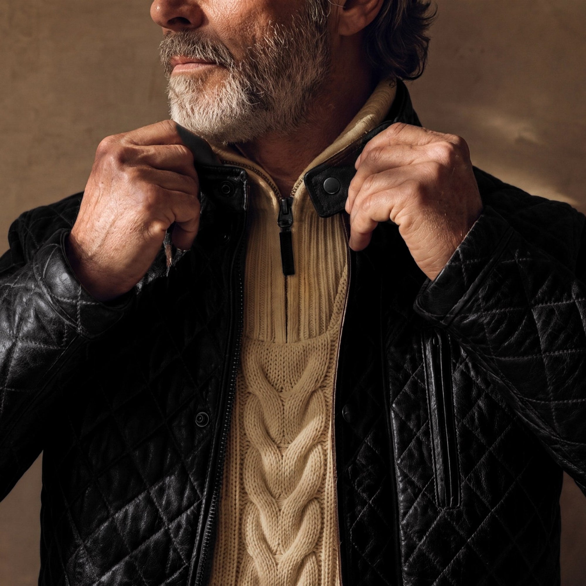 Man fastening the collar of the Highlands Quilted Leather Jacket in Black over a cream cable-knit sweater.