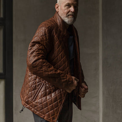 Man in the Highlands Quilted Leather Jacket in Whiskey Brown against a concrete wall.