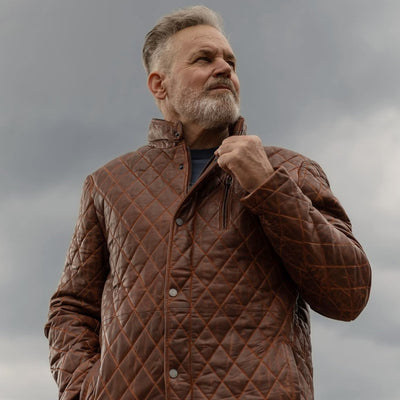 Man in the Highlands Quilted Leather Jacket in Whiskey Brown on a rooftop under a stormy sky.