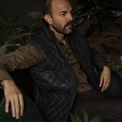 Man seated in an armchair in the Highlands Quilted Leather Vest in Black.