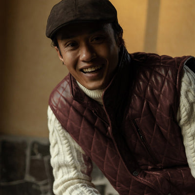 Man laughing in the Highlands Quilted Leather Vest in Mahogany Brown over a cream cable-knit sweater.