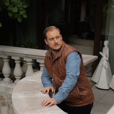 Man leaning on a balustrade in the Highlands Quilted Leather Vest in Whiskey Brown.