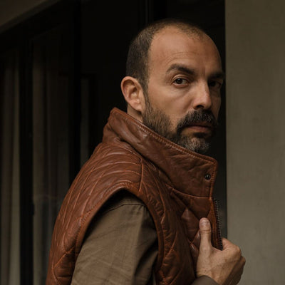 Man in the Highlands Quilted Leather Vest in Whiskey Brown, turning in a doorway.