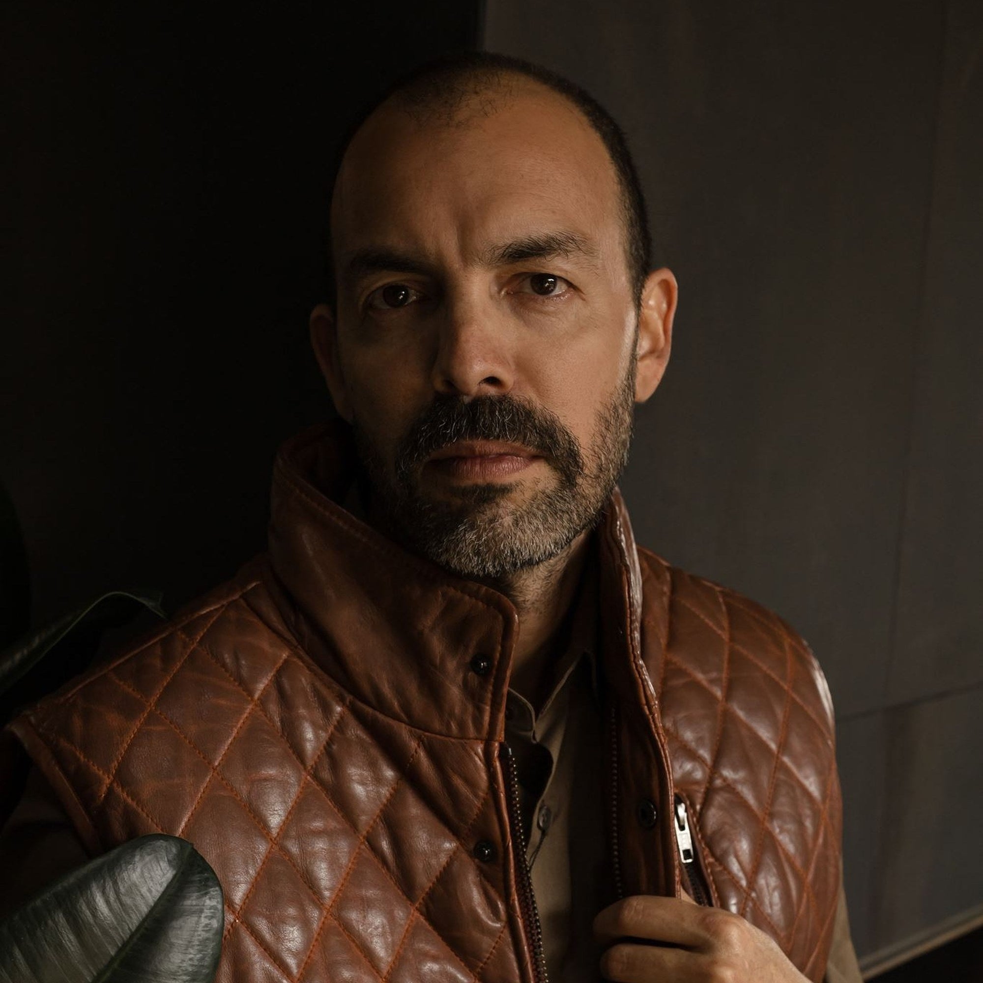 Close portrait of a man in the Highlands Quilted Leather Vest in Whiskey Brown, holding the collar.