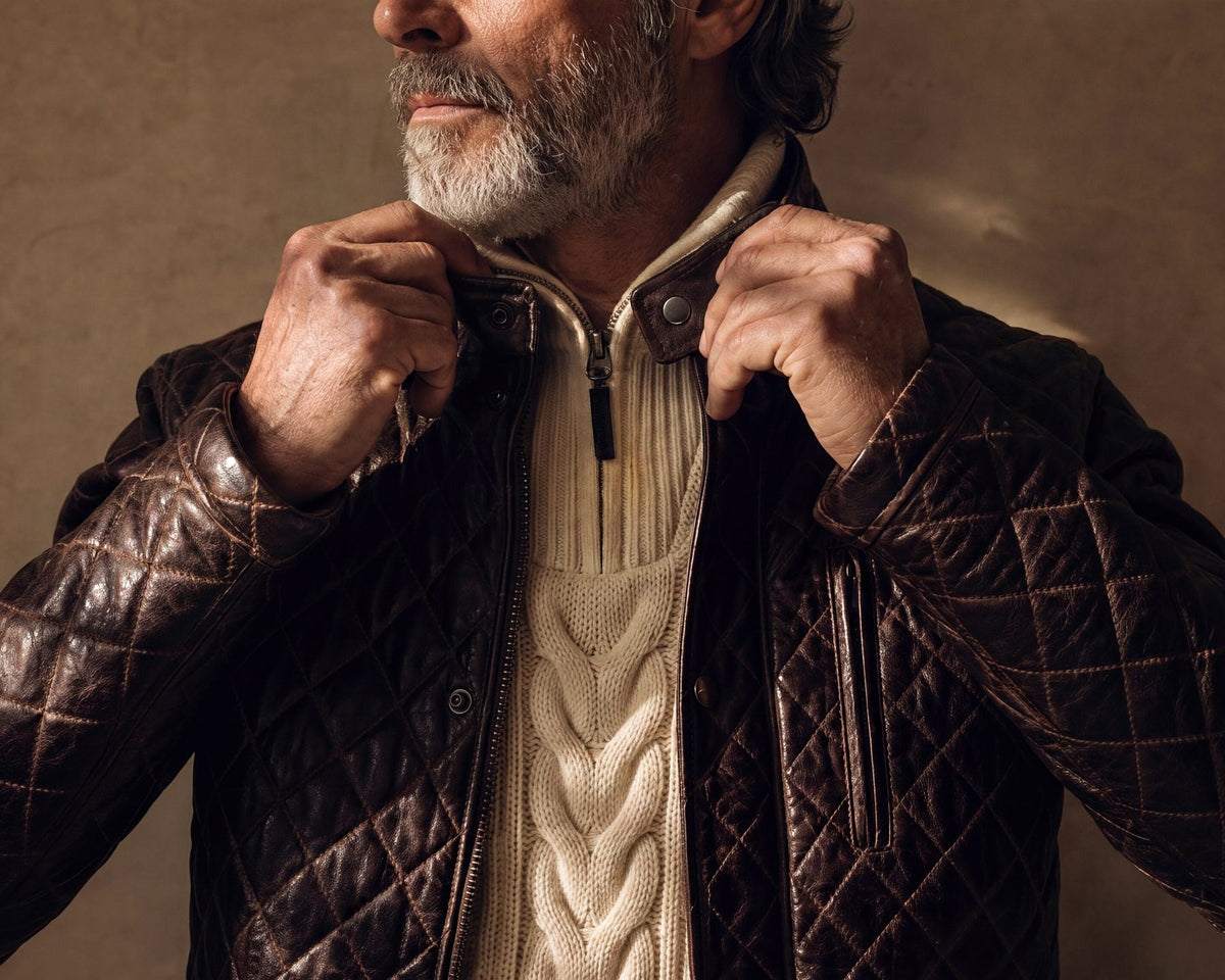 Close view of a man adjusting the collar of a mahogany quilted leather jacket over a cream knit