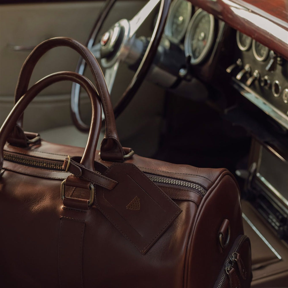 Brown leather duffle on the seat of a vintage car beside the steering wheel