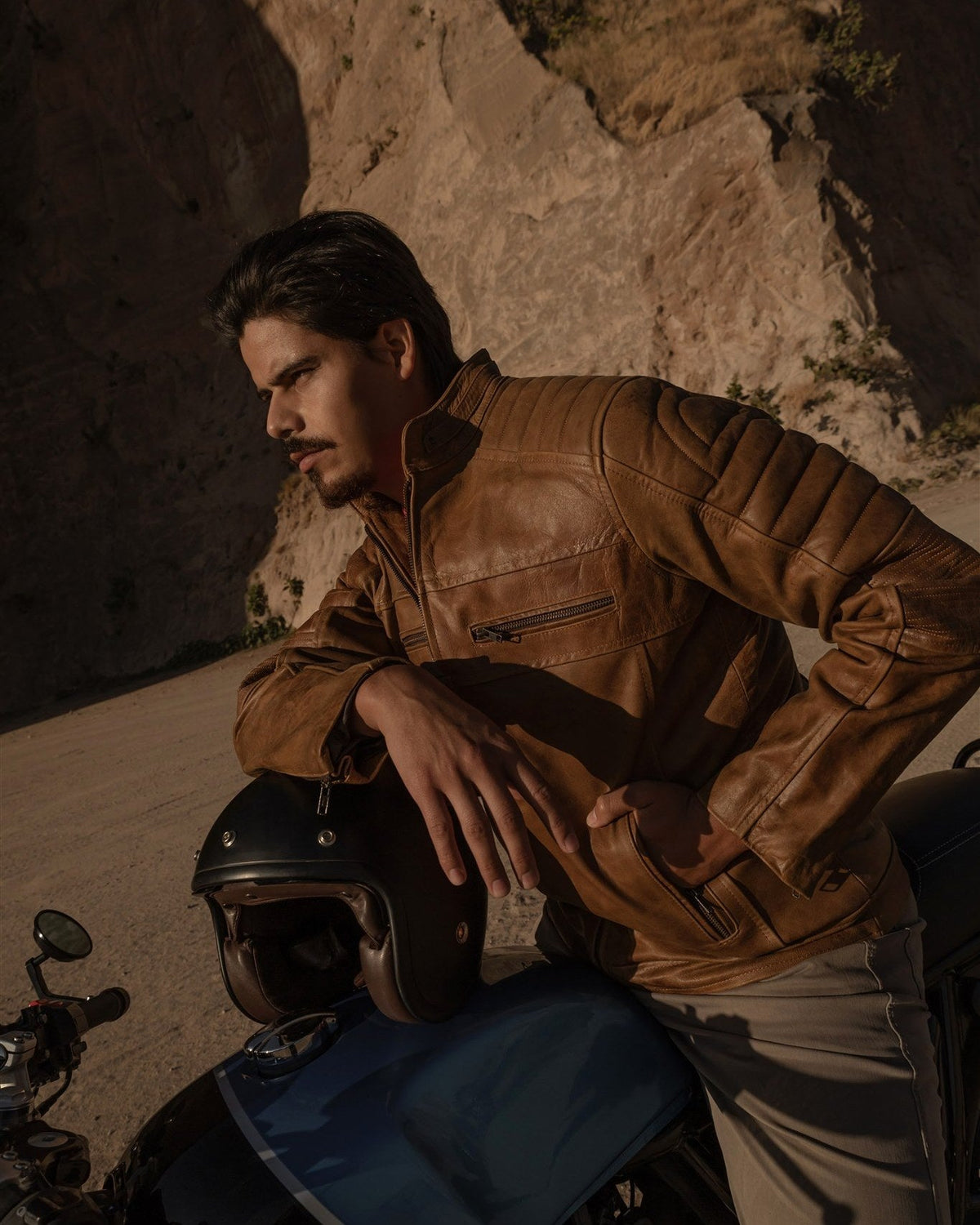 Man in the Cafe Racer Leather Jacket in Distressed Tan leaning on a motorcycle in the desert