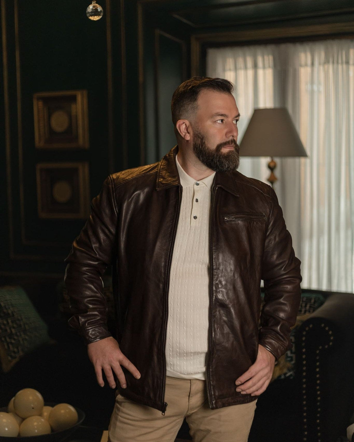 Man in the Glenwood Leather Driving Jacket in Mahogany Brown standing in a dark green sitting room