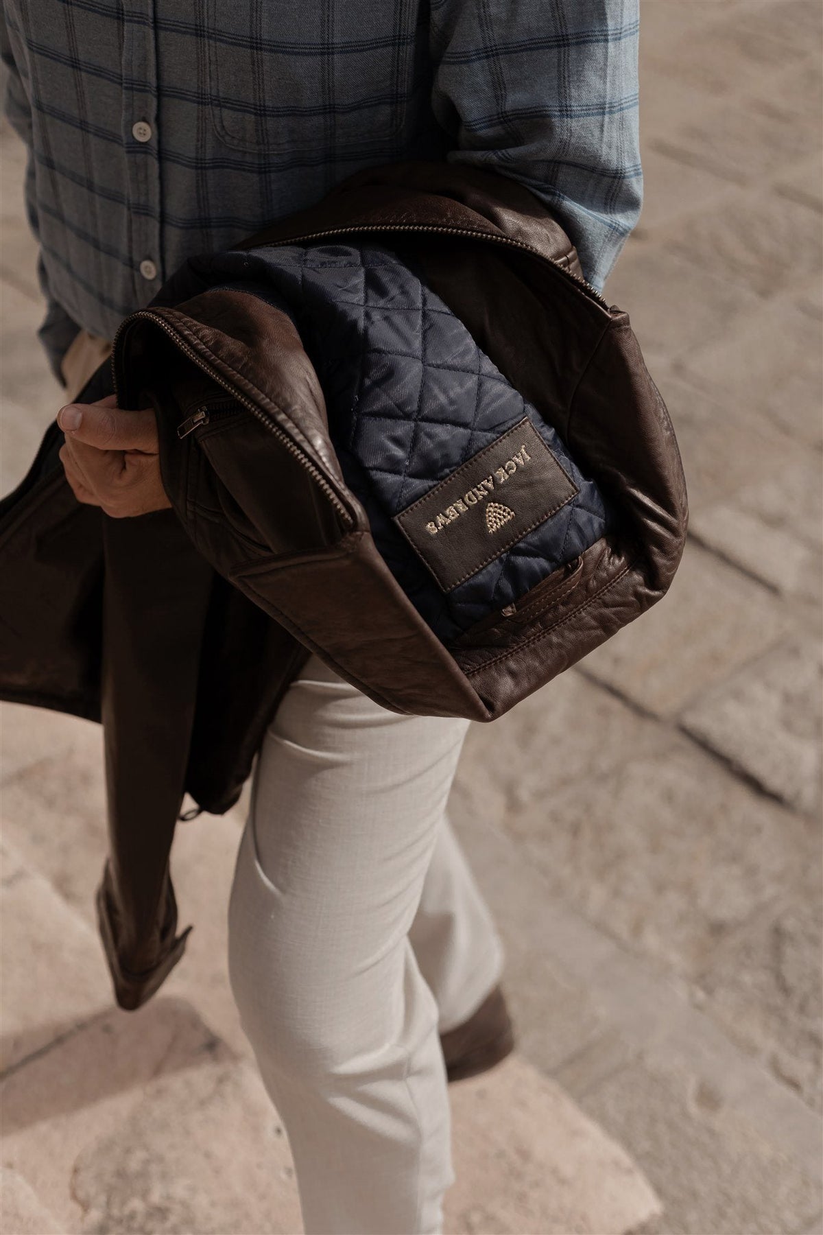 Man carrying a brown Jack Andrews leather jacket, the label on the navy quilted lining in view.
