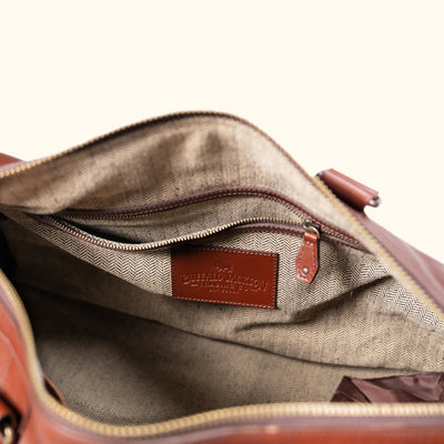 Close-up view of an unzipped tan leather duffle bag, showcasing the spacious lined interior and intricate stitching details.