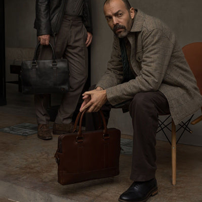 Seated man with the Jefferson Leather Attaché Briefcase in Elderwood Brown, beside a man holding the Vintage Black.