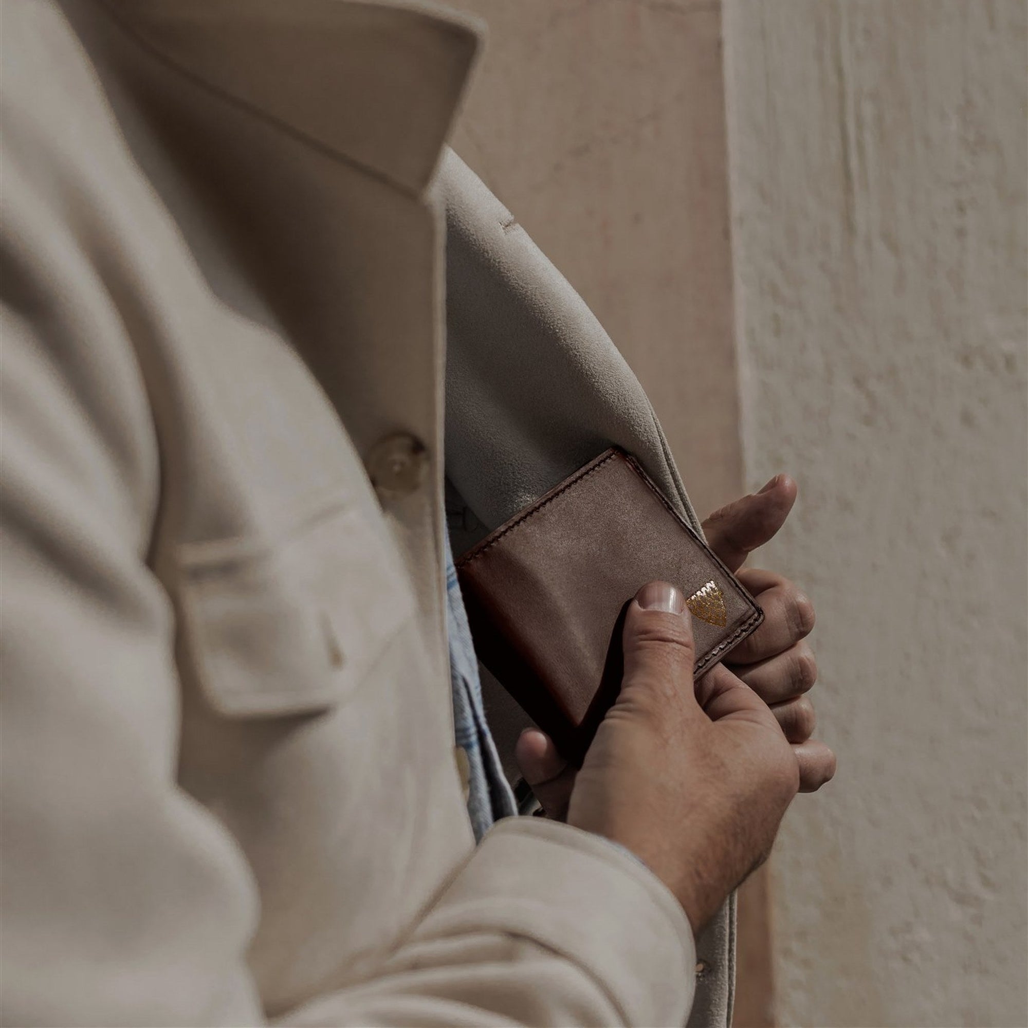 Man slipping the Jefferson Leather Bifold Wallet in Elderwood Brown into his jacket pocket.