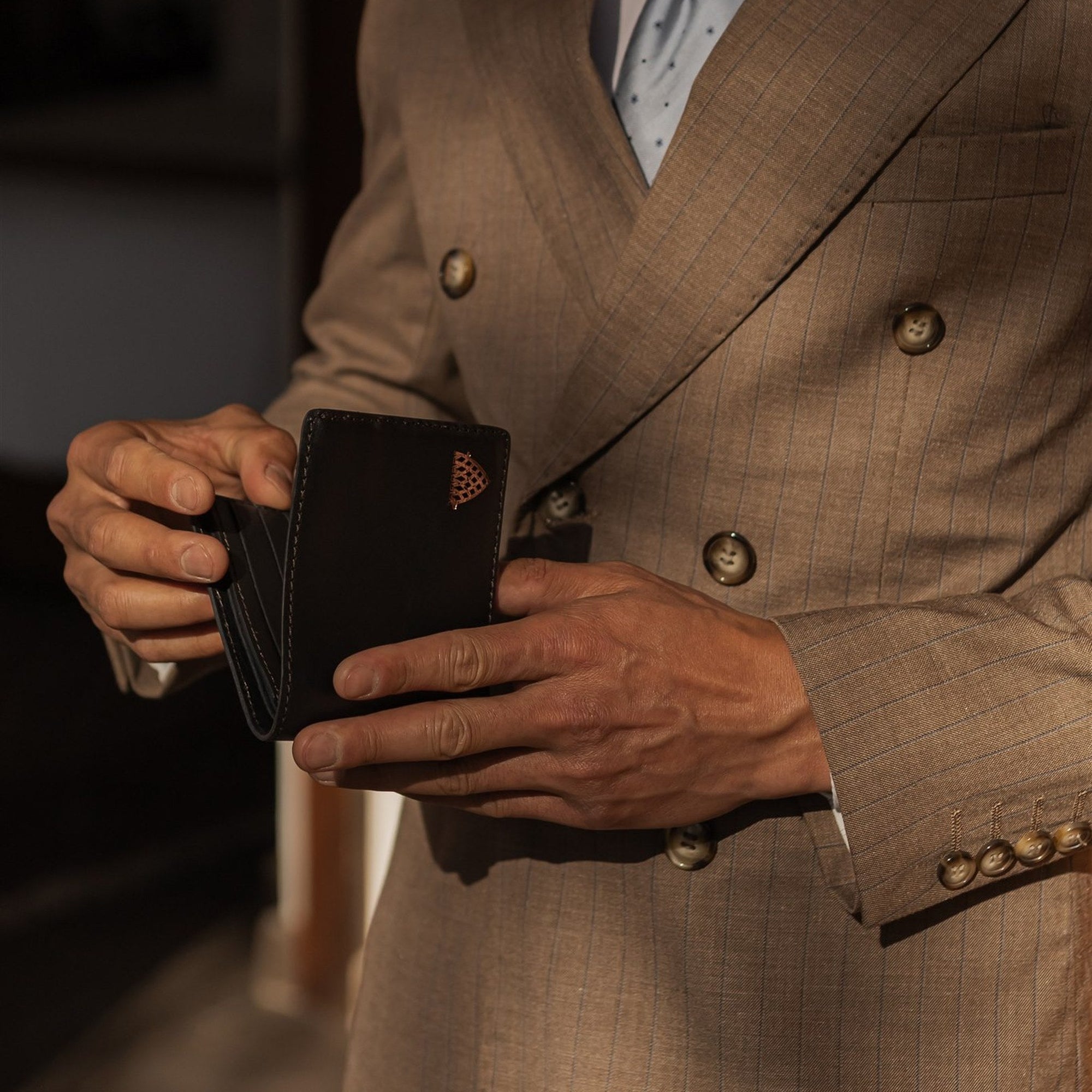 Man in a tan double-breasted suit holding the Jefferson Leather Bifold Wallet in Vintage Black.