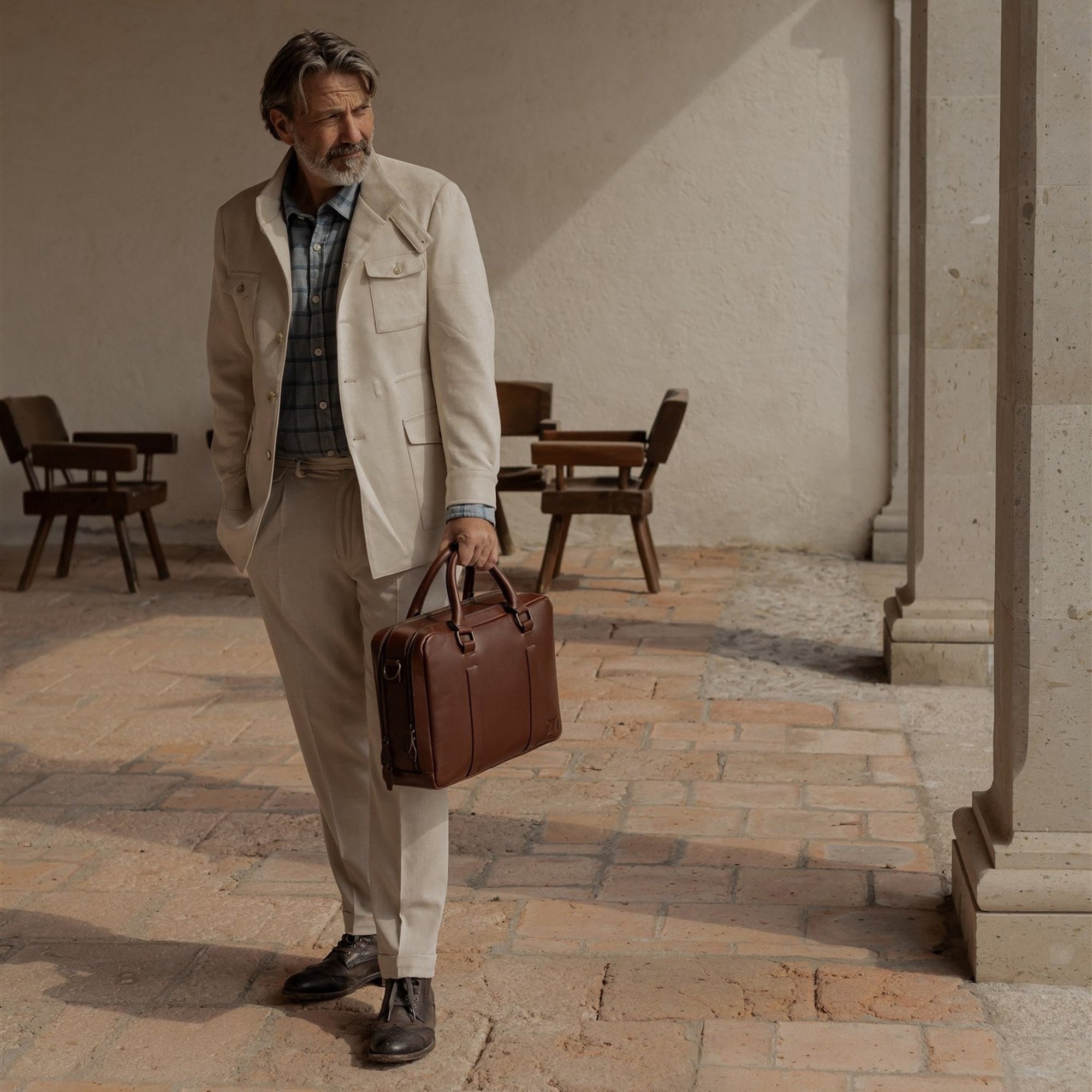 Man walking through a courtyard carrying the Jefferson Leather Briefcase in Elderwood Brown.