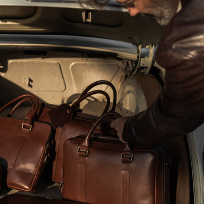 Man loading the Jefferson Leather Briefcase in Elderwood Brown into a vintage car trunk.
