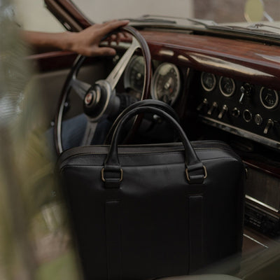 The Jefferson Leather Briefcase in Vintage Black on the seat beside the driver of a vintage car.