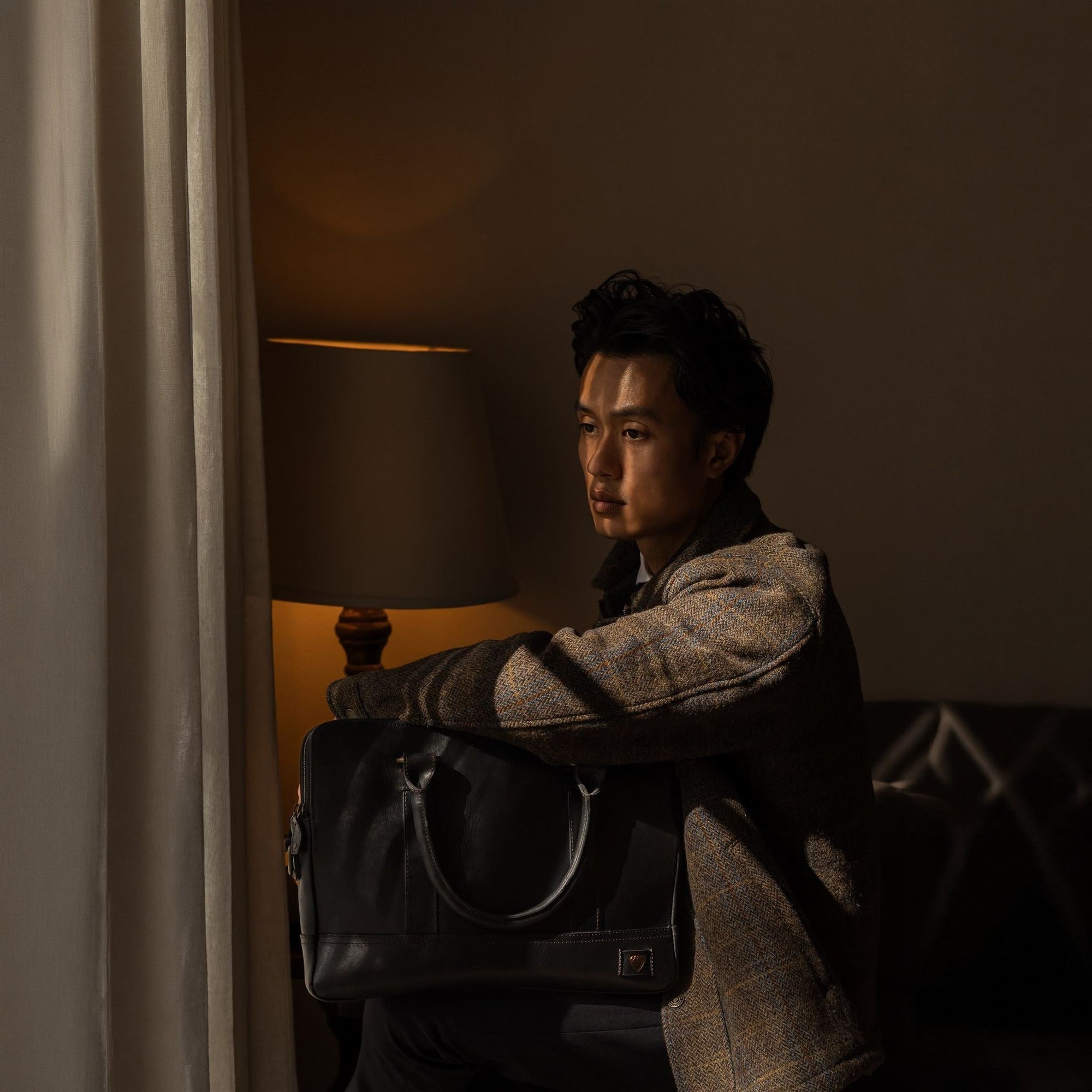 Man in a tweed jacket seated by lamplight with the Jefferson Leather Briefcase in Vintage Black.