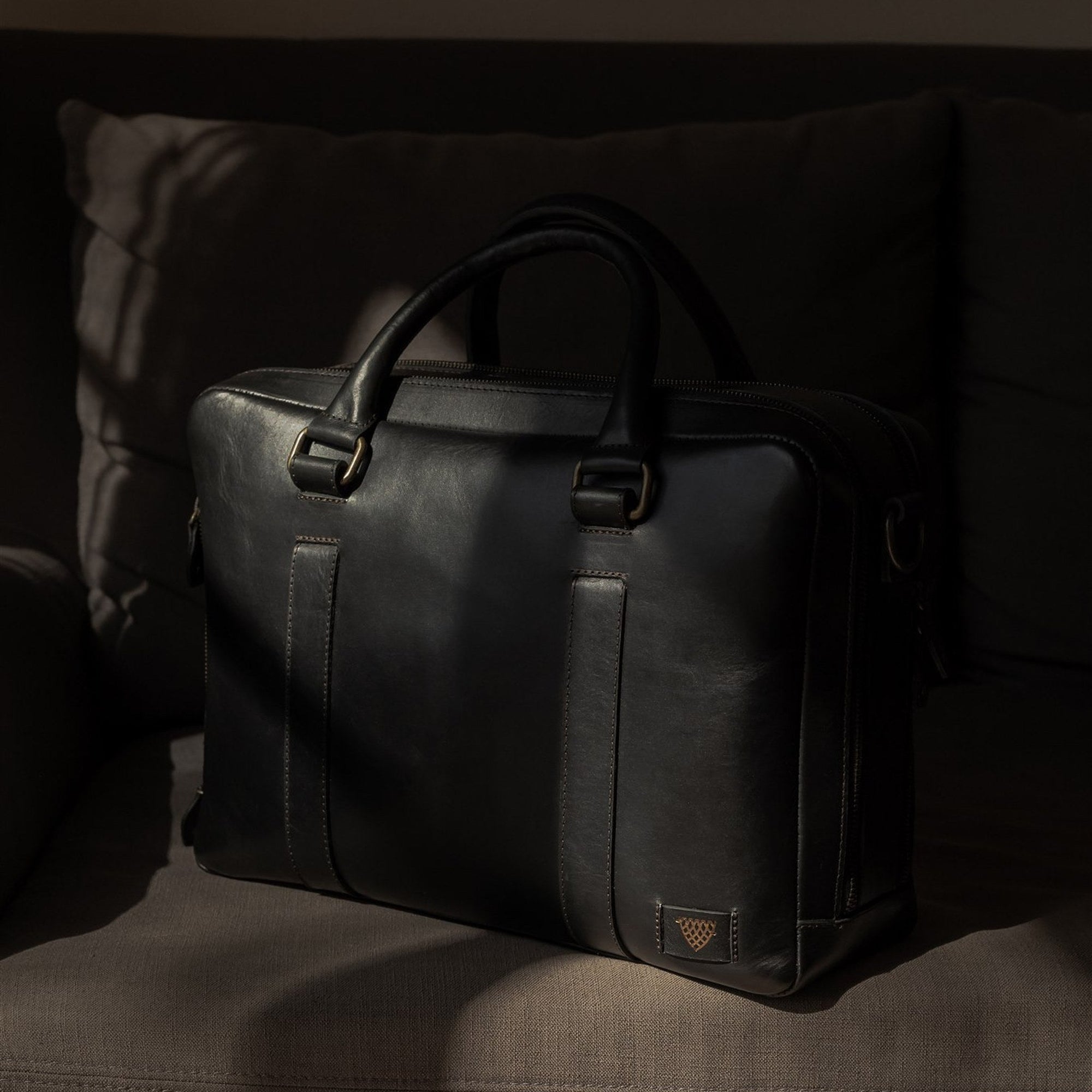 The Jefferson Leather Briefcase in Vintage Black resting on a sofa in window light.