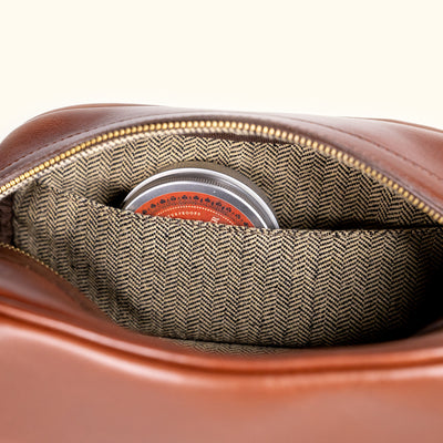 Detailed look inside a leather bag, showcasing herringbone fabric lining and a zippered section.