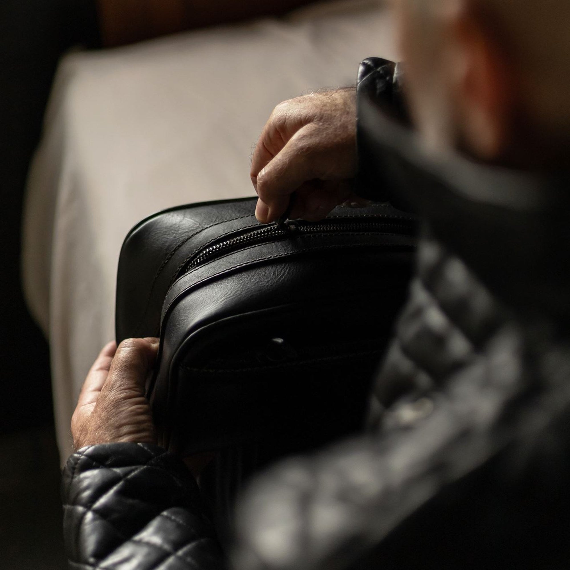Man lifting the Jefferson Leather Dopp Kit in Vintage Black off a bed.