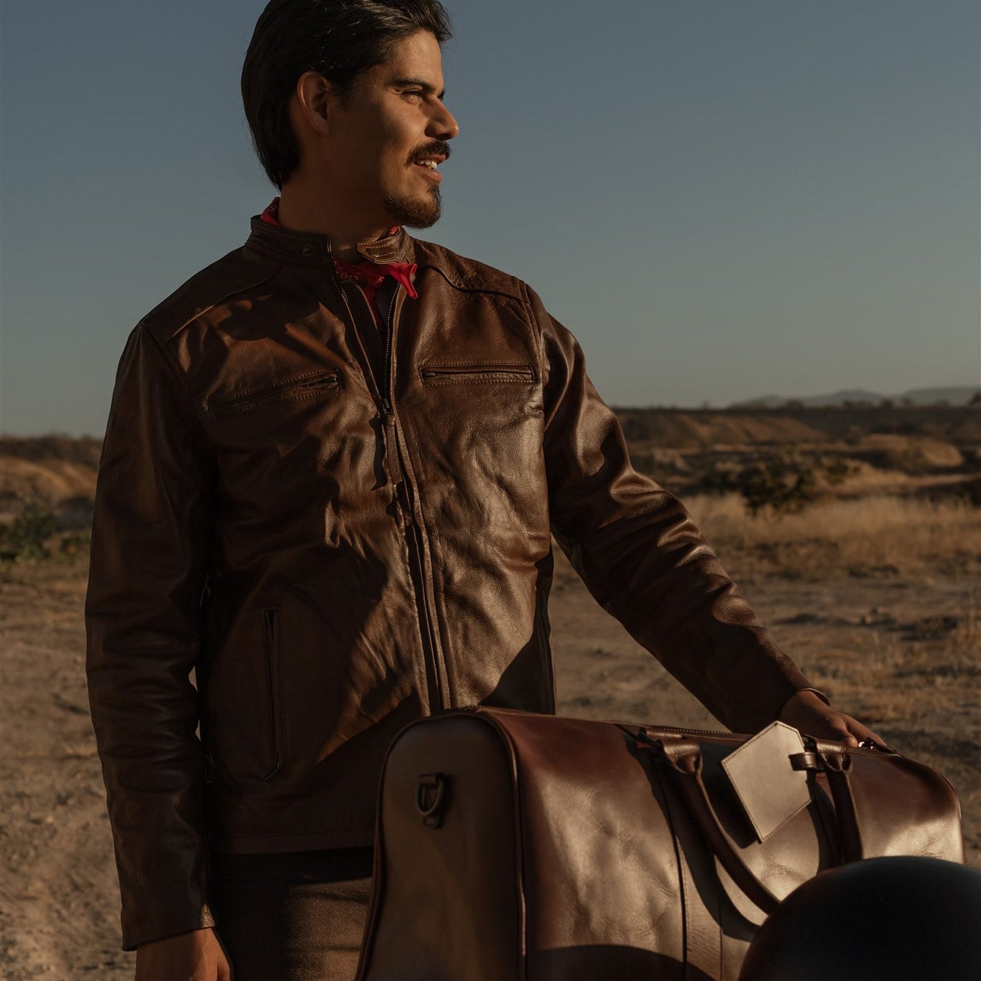 Man standing beside the Jefferson Leather Duffle in Elderwood Brown in the desert at golden hour.