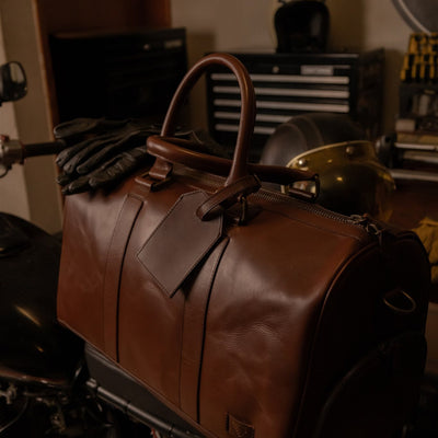 Jefferson Leather Duffle in Elderwood Brown resting on a motorcycle seat in a garage.