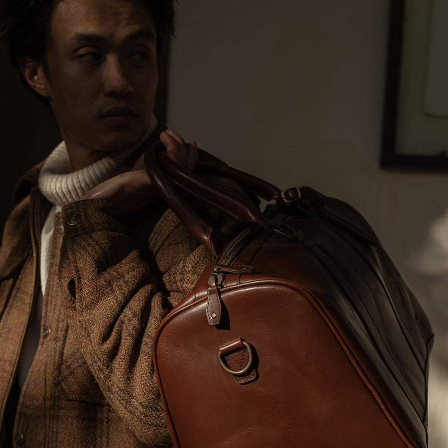 Jefferson Leather Duffle in Elderwood Brown, front three-quarter view with shoulder strap and luggage tag.