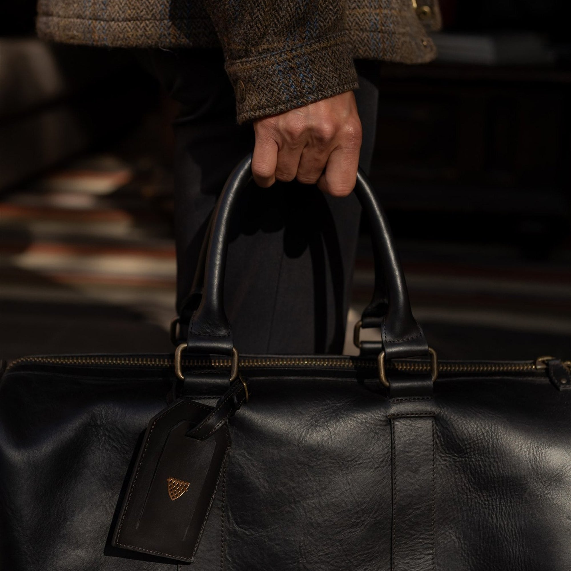 Jefferson Leather Duffle in Vintage Black carried by the handles, luggage tag in view.