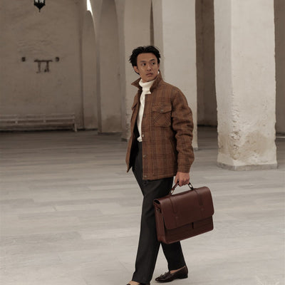 Man walking through a white arcade carrying the Jefferson Leather Messenger Bag in Elderwood Brown.