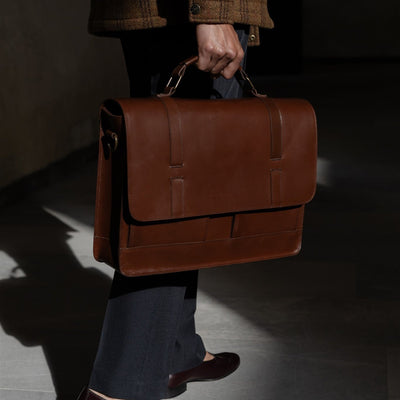 Man carrying the Jefferson Leather Messenger Bag in Elderwood Brown by its top handle.