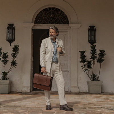Man in a cream linen suit in a doorway with the Jefferson Leather Messenger Bag in Elderwood Brown.