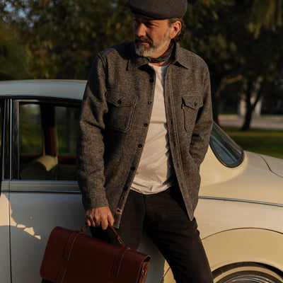 Man in a flat cap by a vintage car with the Jefferson Leather Messenger Bag in Elderwood Brown.