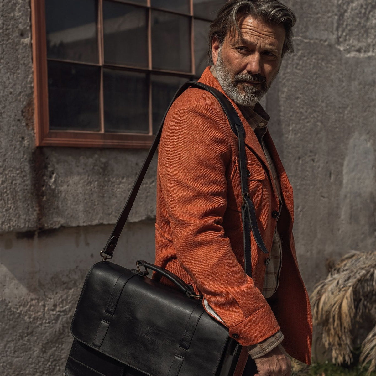 Man in an orange jacket wearing the Jefferson Leather Messenger Bag in Vintage Black on his shoulder.
