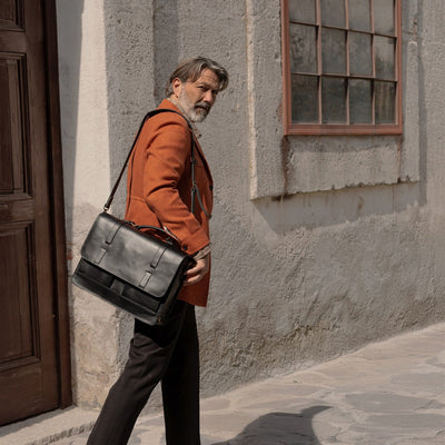 Man walking past a stone wall with the Jefferson Leather Messenger Bag in Vintage Black.